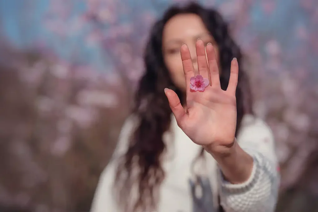 A woman holds up her hand with a single pink flower resting on it.