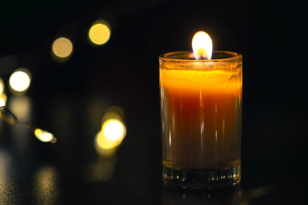 Photo of a single lit orange candle against a background of soft, out-of-focus lights, creating a reflective mood for a sensitive topic.
