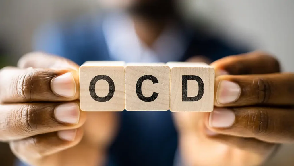 A direct and clear image of a person's hands holding up four wooden blocks that spell the acronym 'OCD'.