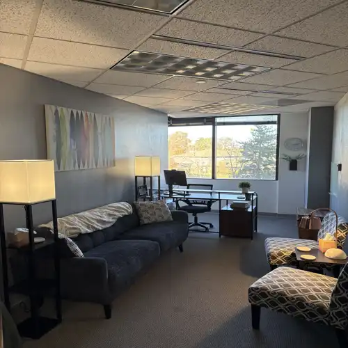 Modern therapy Austin office in Longmont interior with a navy blue sofa, patterned armchairs, and a desk near a large window.