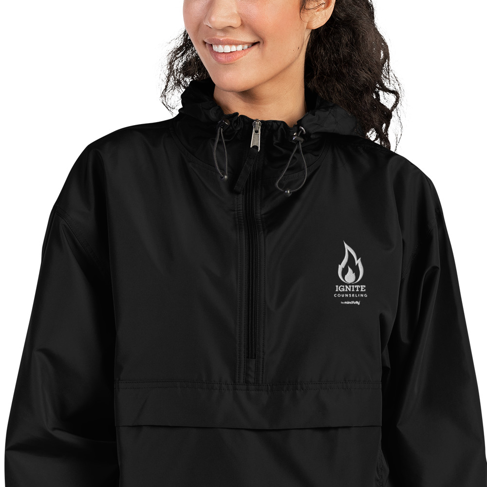 Close-up of a smiling woman modeling a black windbreaker featuring the Ignite Counseling logo.