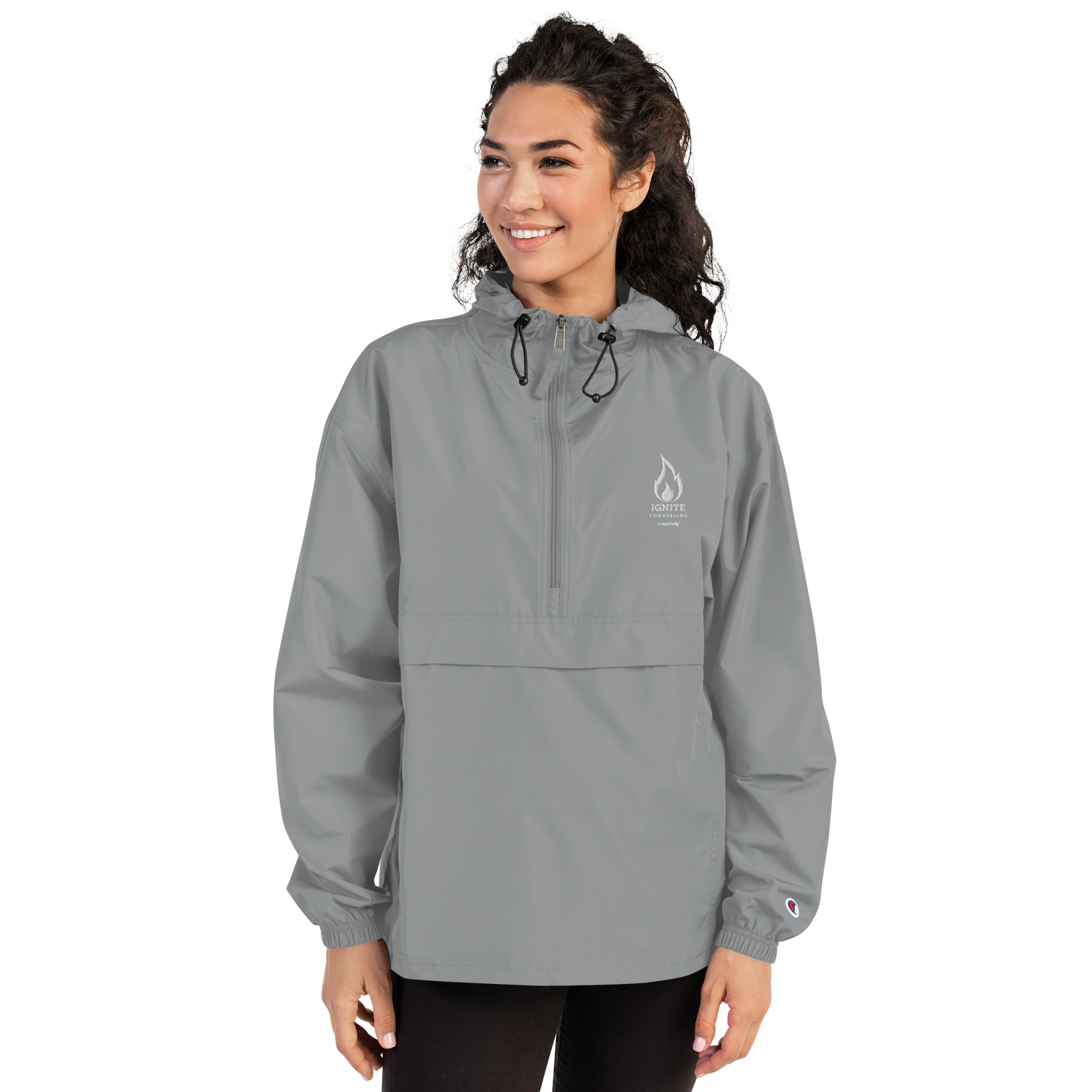 Smiling woman modeling a grey windbreaker jacket featuring the Ignite Counseling logo.