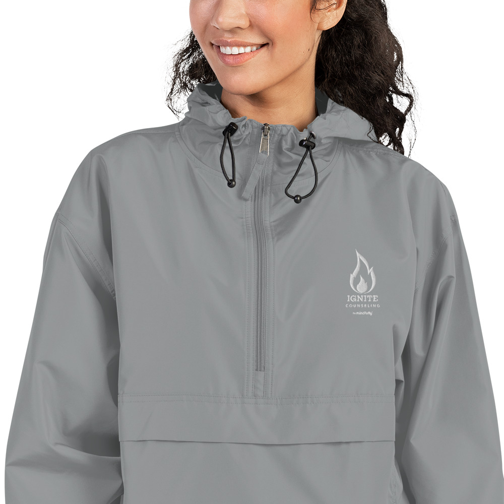 Close-up of a smiling woman modeling a grey windbreaker featuring the Ignite Counseling logo.