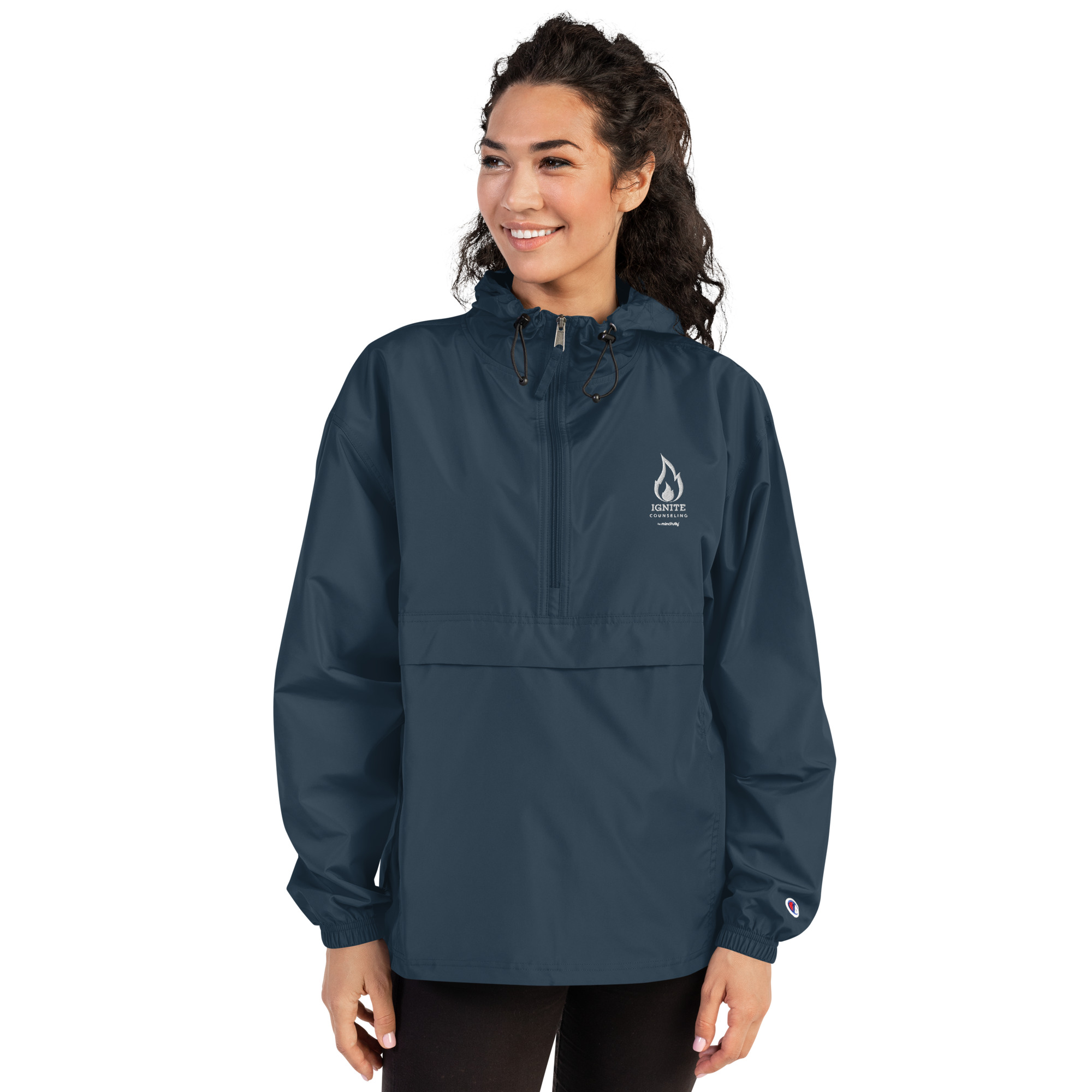 Smiling woman modeling a navy blue windbreaker jacket featuring the Ignite Counseling logo.