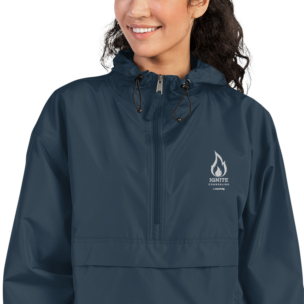 Close-up of a smiling woman modeling a navy blue windbreaker featuring the Ignite Counseling logo.