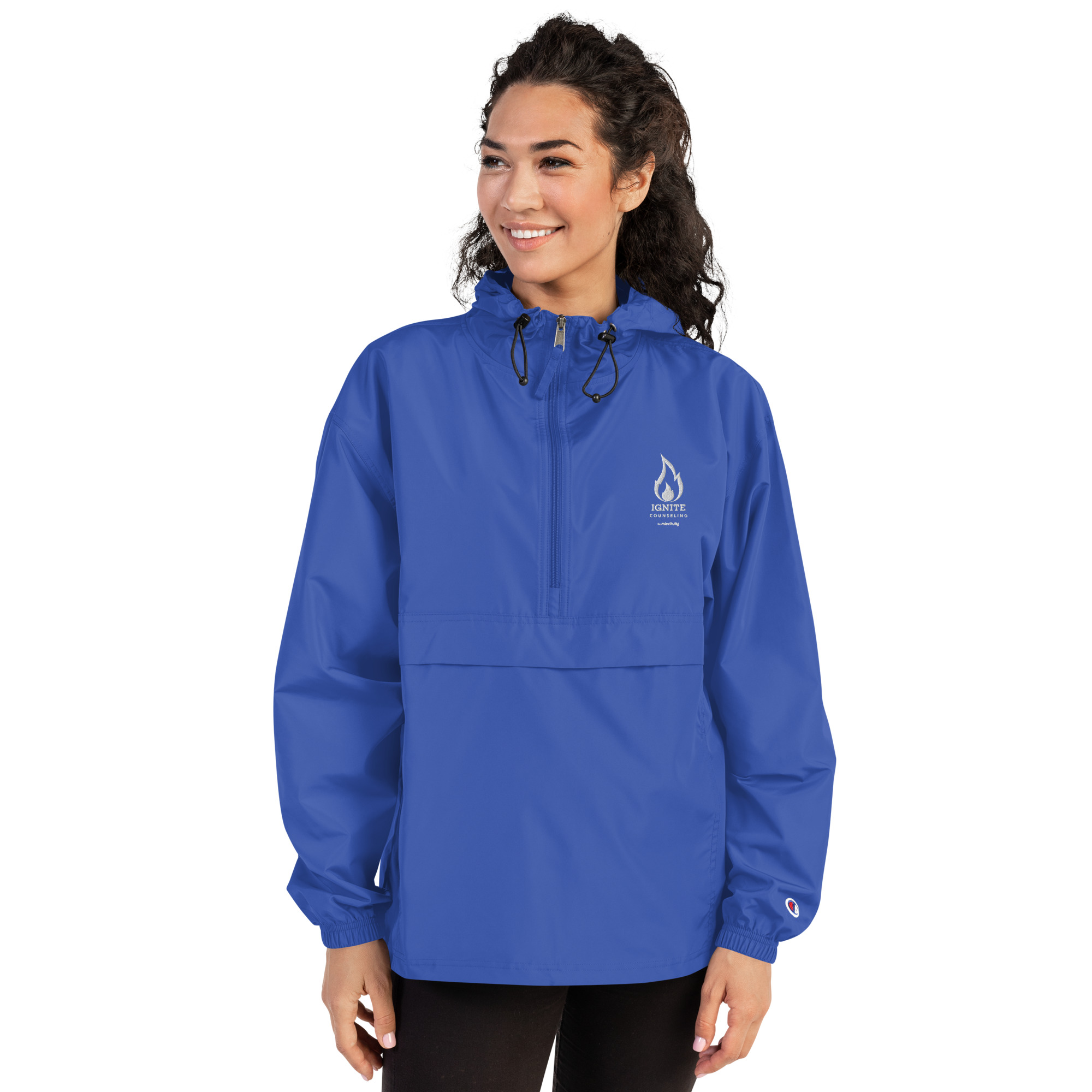 Smiling woman modeling a royal blue windbreaker jacket featuring the Ignite Counseling logo.