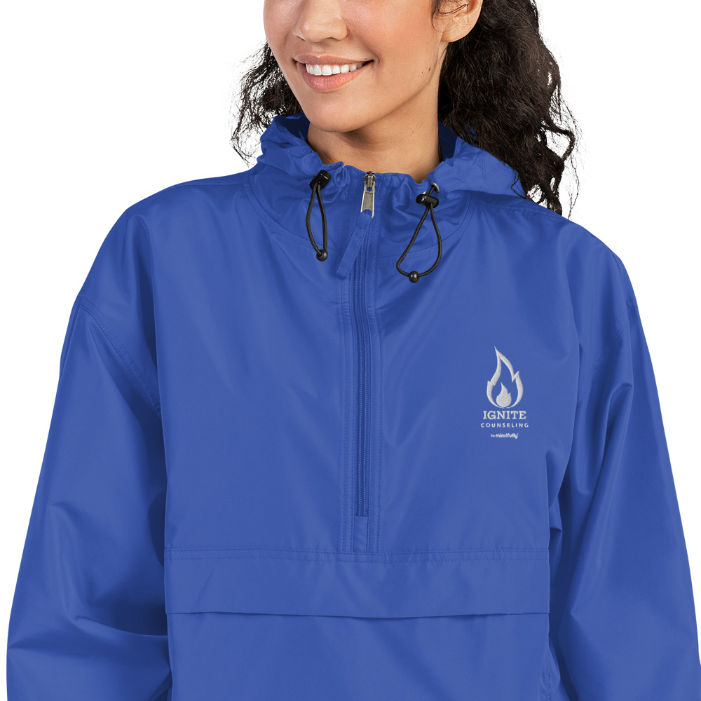 Close-up of a smiling woman modeling a royal blue windbreaker featuring the Ignite Counseling logo.