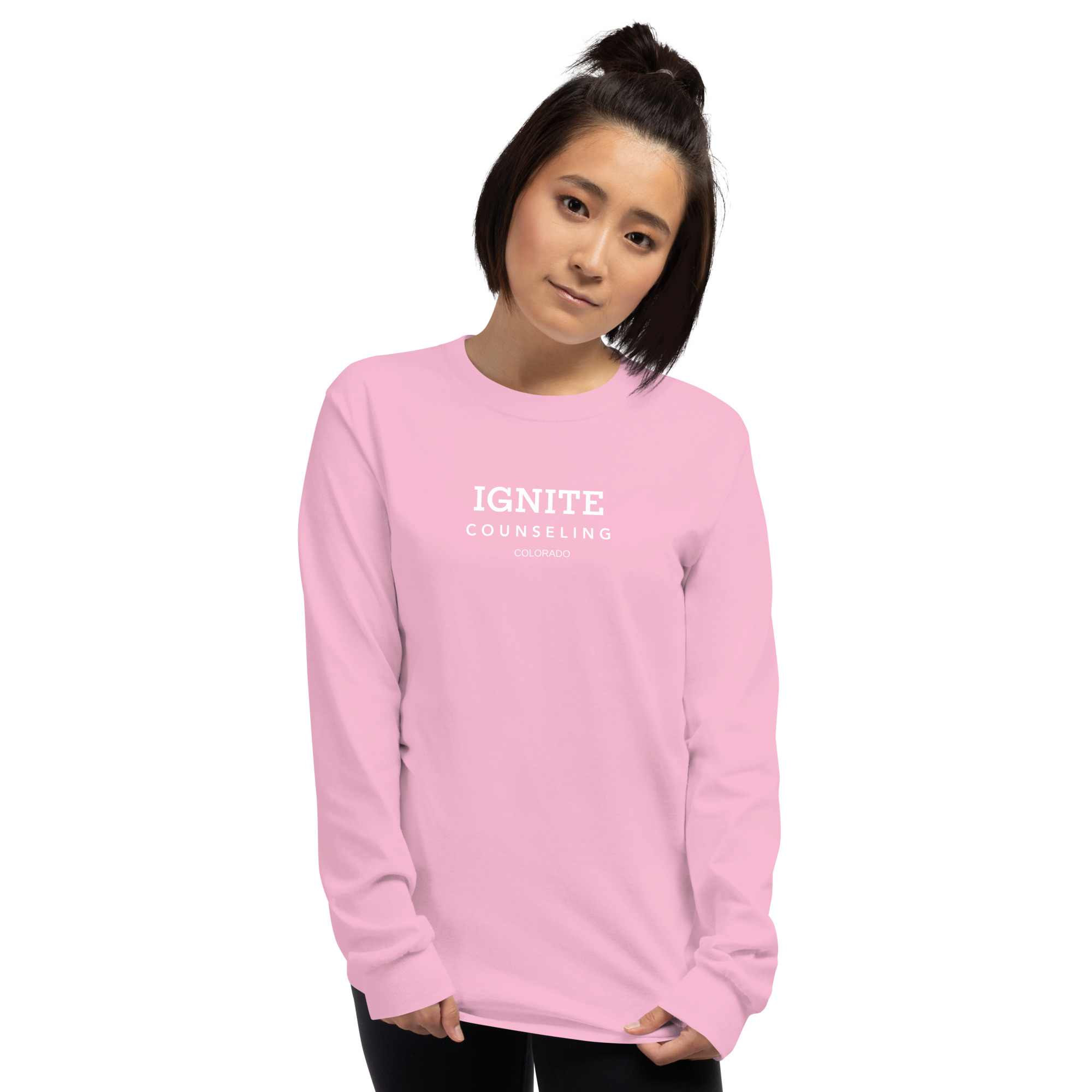 Woman modeling a light pink long-sleeve t-shirt featuring the Ignite Counseling Colorado logo.