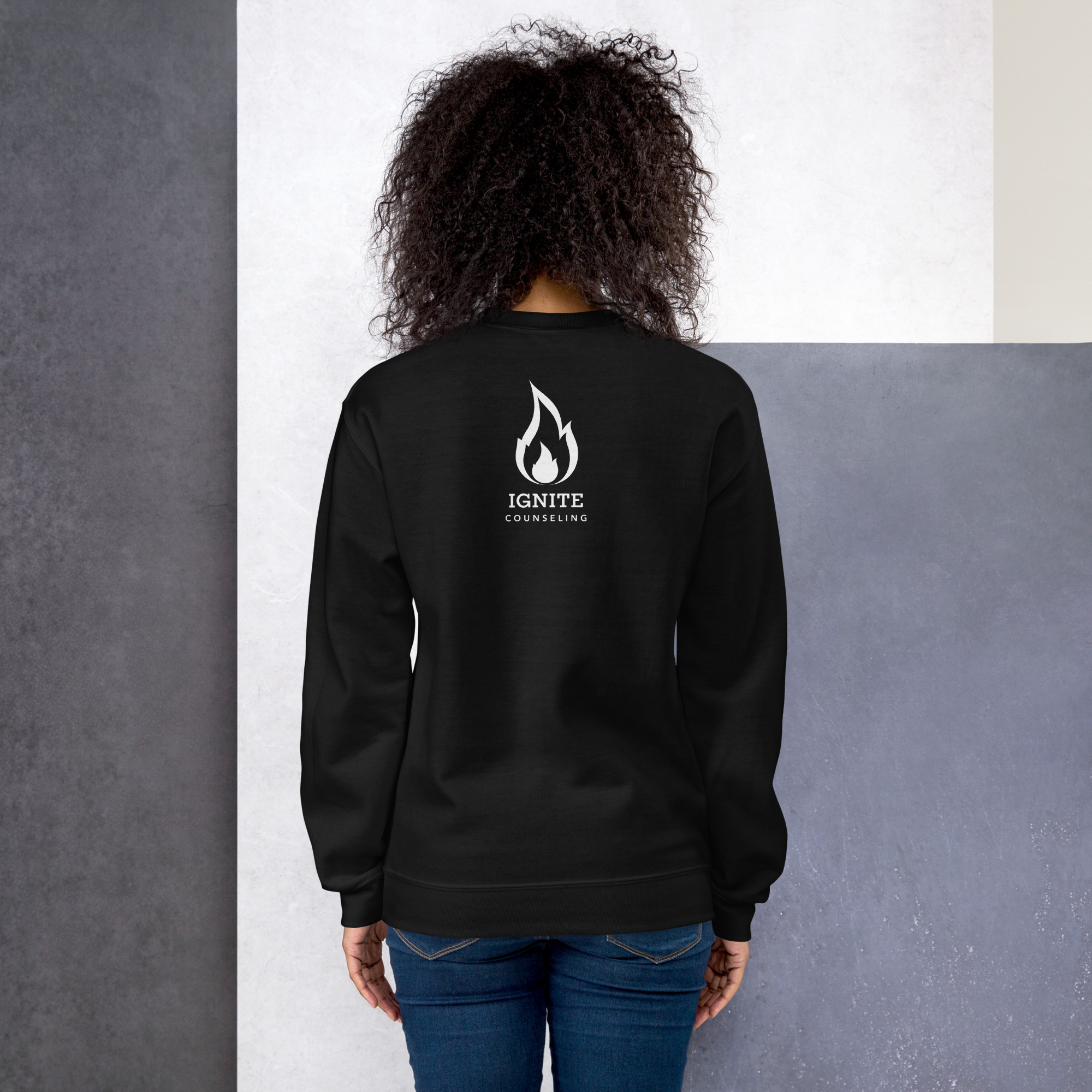 Back view of a model wearing a black sweatshirt featuring the white Ignite Counseling logo.