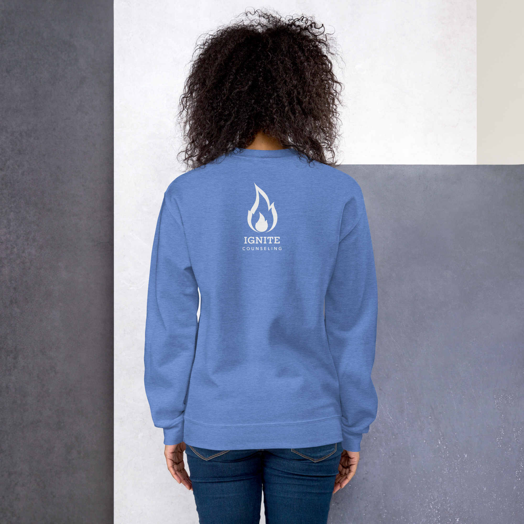Back view of a model wearing a light blue sweatshirt featuring the white Ignite Counseling logo.