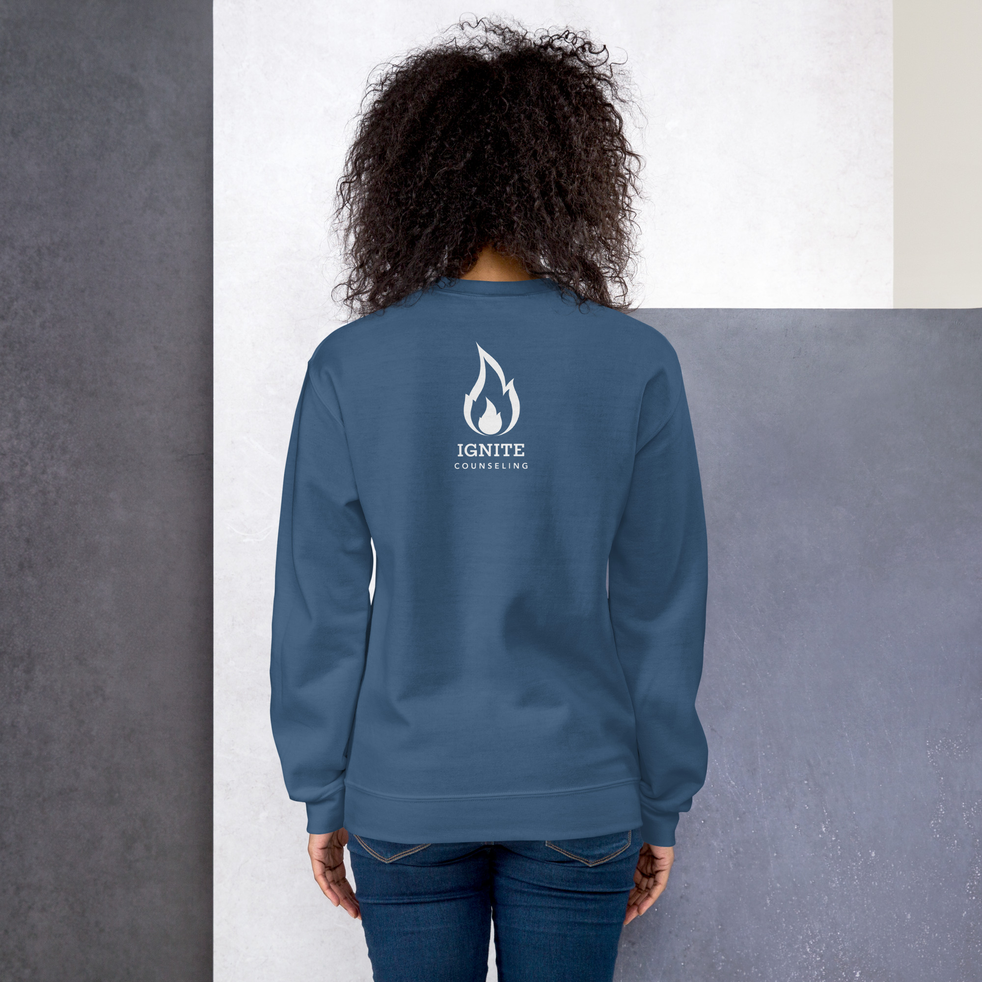 Back view of a model wearing a heather blue sweatshirt featuring the white Ignite Counseling logo.