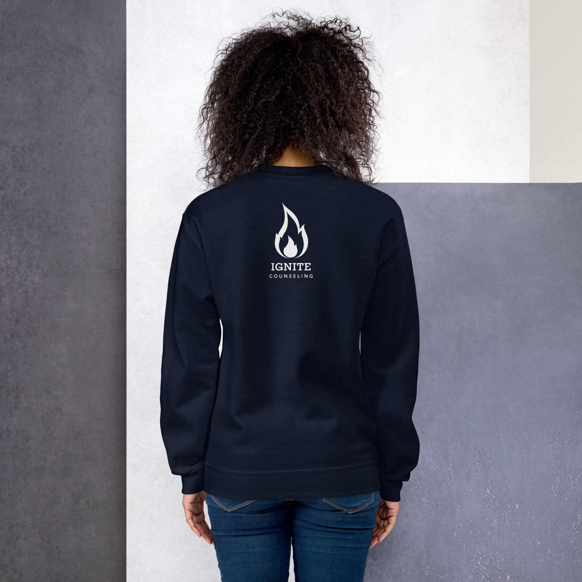 Back view of a model wearing a navy blue sweatshirt featuring the white Ignite Counseling logo.