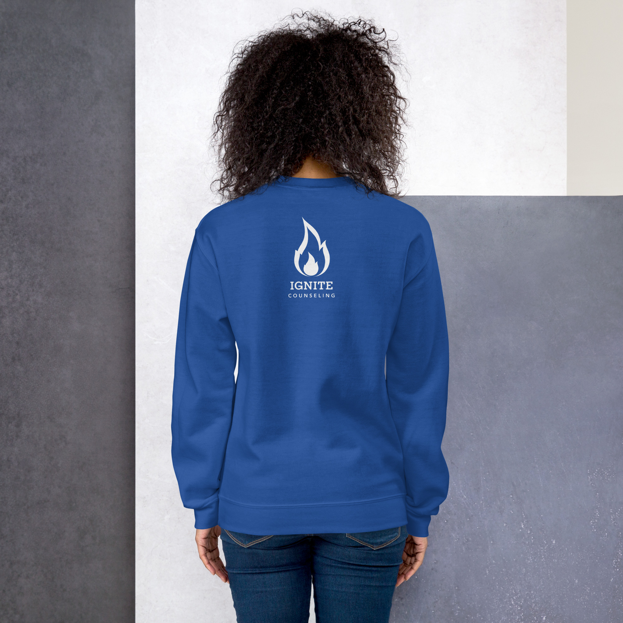 Back view of a model wearing a royal blue sweatshirt featuring the white Ignite Counseling logo.
