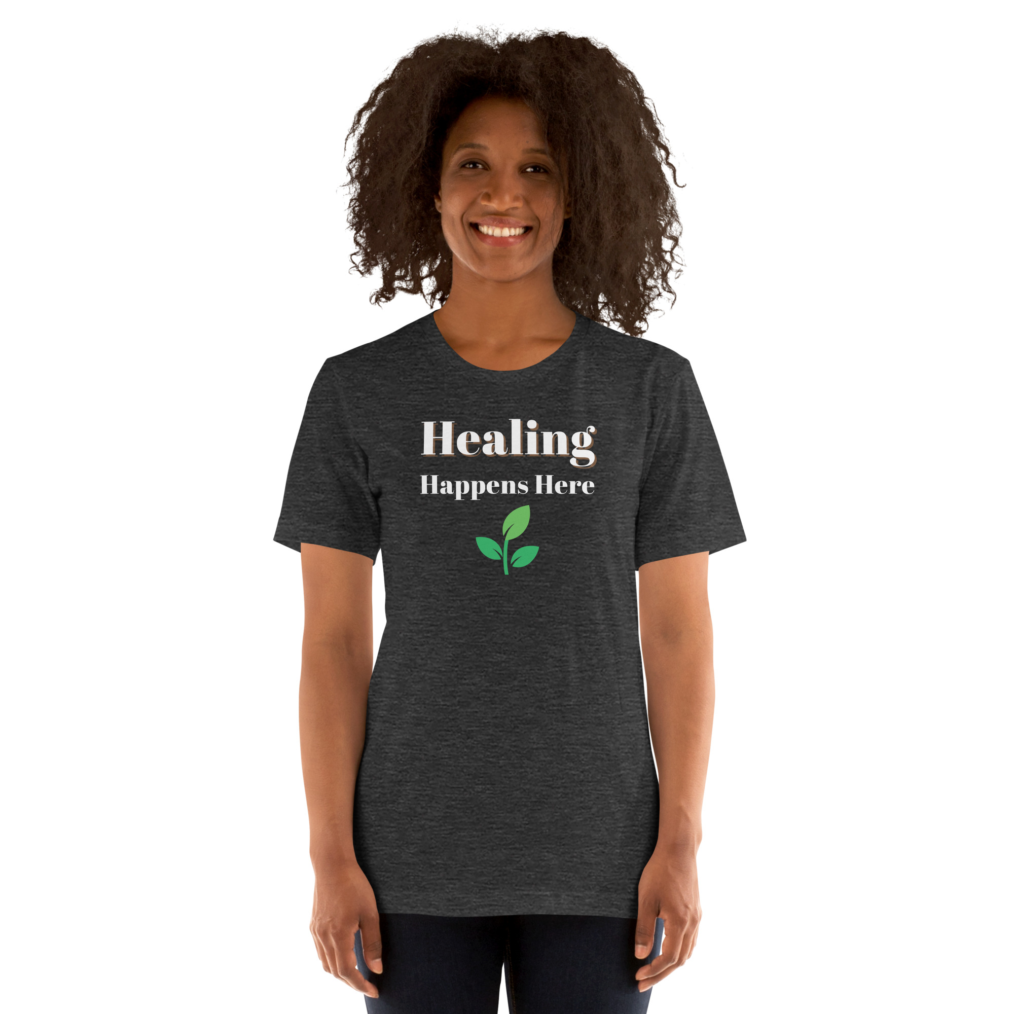 Smiling woman modeling a heather dark grey t-shirt featuring the text 'Healing Happens Here' and a green leaf graphic.