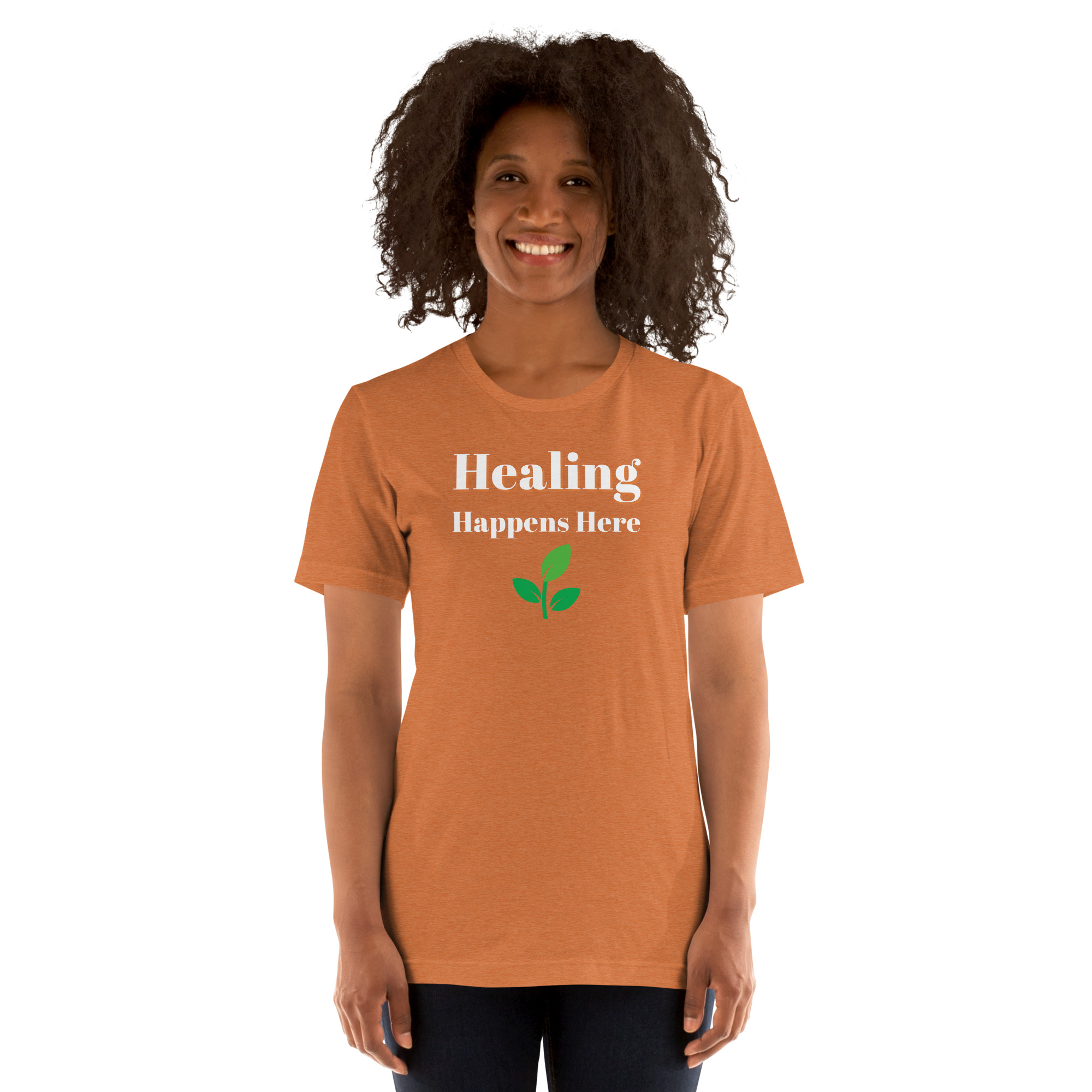 Smiling woman modeling a heather orange t-shirt featuring the text 'Healing Happens Here' and a green leaf graphic.