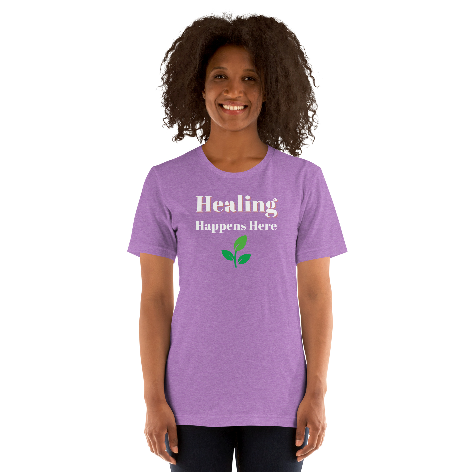 Smiling woman modeling a heather purple t-shirt featuring the text 'Healing Happens Here' and a green leaf graphic.