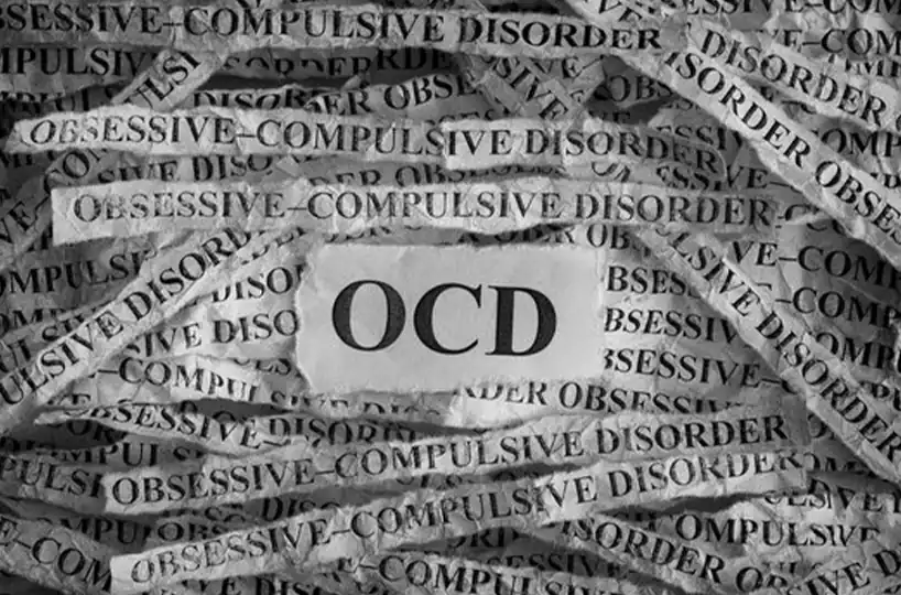 The letters "OCD" on a torn piece of paper, surrounded by strips of paper repeating "OBSESSIVE-COMPULSIVE DISORDER," symbolizing the weight of the condition.