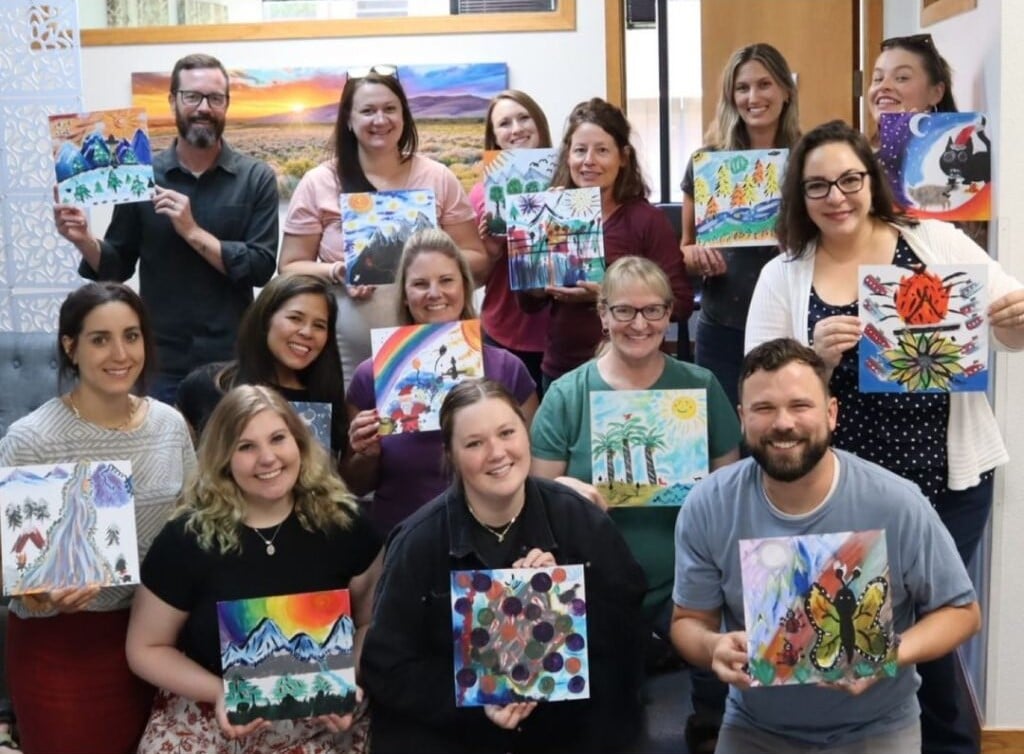 Therapy Austin team members smiling and displaying their colorful artwork during a creative group activity.
