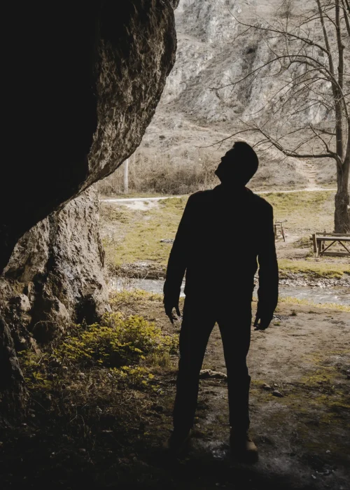 Silhouette of a person standing in a shadowed cave looking out toward a bright landscape, representing the journey of finding hope through mental health support.